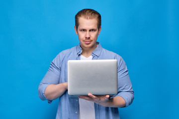 A man in a blue shirt holds a laptop and looks at the camera. Programmer concept working on...