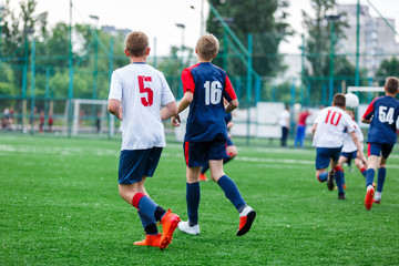 Obraz na płótnie Canvas Boys in white and blue sportswear plays football on field, dribbles ball. Young soccer players with ball on green grass. Training, football, active lifestyle for kids concept 