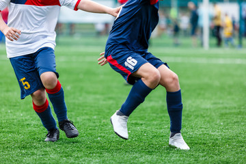 Boys in white and blue sportswear plays  football on field, dribbles ball. Young soccer players with ball on green grass. Training, football, active lifestyle for kids concept 