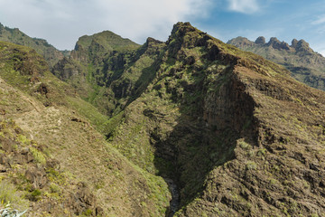Aerial view of famous Hell gorge in Adeje. Sunny day. Blue sky and clouds above the mountains. Rocky tracking road in dry mountain area. Tenerife, Canary Islands