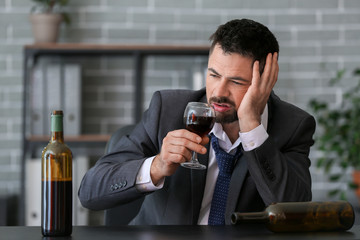 Businessman drinking wine in office. Concept of alcoholism