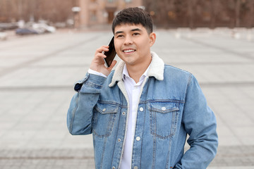 Young Asian man talking by mobile phone outdoors