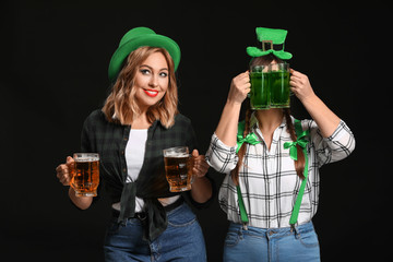 Funny young women with beer on dark background. St. Patrick's Day celebration