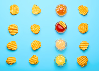 Tasty potato chips and sauces on color background