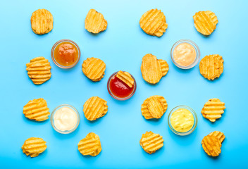 Tasty potato chips and sauces on color background