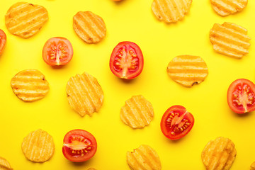 Tasty potato chips and tomato on color background