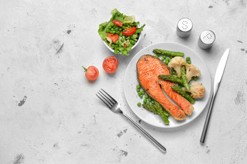 Tasty fried salmon with vegetables and salad on table