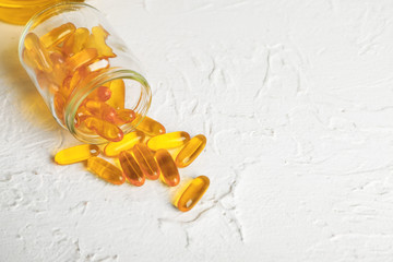 Jar with scattered fish oil pills on white background