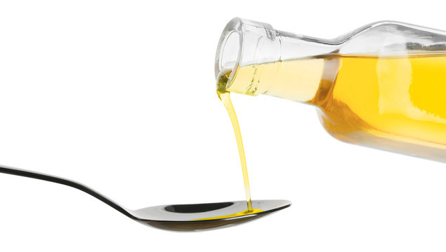 Pouring of fish oil from bottle into spoon against white background