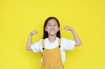 Strong asian little kid girl raising hands up and smiling. Portrait of happy child in dungarees...