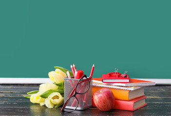 Stationery, bouquet of flowers and apple on table in classroom. Teacher's Day celebration