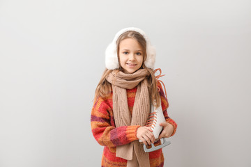 Cute little girl with ice skates on light background