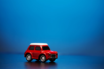 Red colored little toy model car on a blue background.