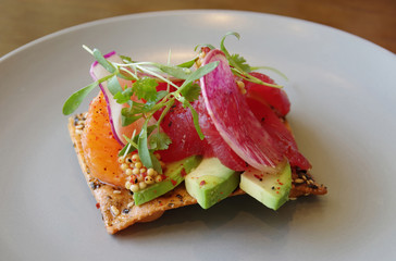 A creative spicy appetizer with raw tuna fish, oranges, avocado, a slice o radish and mustard seeds on a crisp