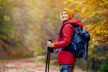 Hiking girl with poles and backpack on a trail. Looking at camera. Travel and healthy lifestyle outdoors in fall season