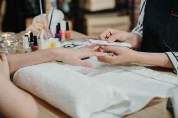 Obraz na płótnie Canvas Hands during manicure care session. focus view on unrecognized asian young lady customer sitting in spa salon applying nail polish from manicurist. beautician doing preparation of nail file on client