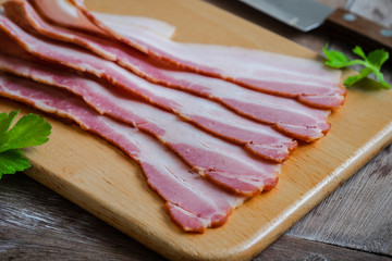 Raw sliced bacon on wooden board.