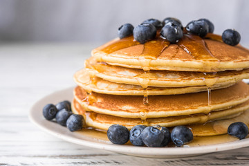 Close up of fluffy pancakes with maple syrup and blueberries against white wooden background