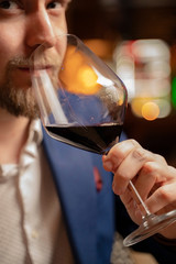 Handsome man extreme closeup, drinking red wine in the club .(Image contains a bit of noise)