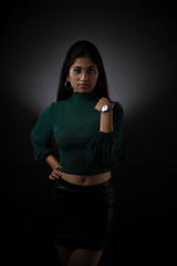 Fashion portrait of an young and attractive Indian Bengali brunette girl with green cropped top, skirt and spectacles in front of a black studio background. Indian fashion portrait and lifestyle.