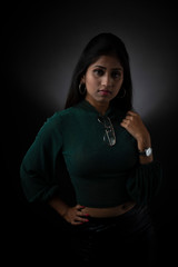 Fototapeta na wymiar Fashion portrait of an young and attractive Indian Bengali brunette girl with green cropped top, skirt and spectacles in front of a black studio background. Indian fashion portrait and lifestyle.
