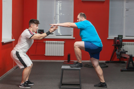 Fat man is diligently doing step-up exercise under control of a personal instructor. Overweight - Powered by Adobe