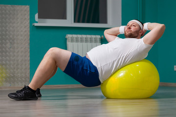 Fototapeta na wymiar Overweight man is lying on a fitness ball during group fitness classes. Fat man looks disappointed because of bad result of weight loss trainings