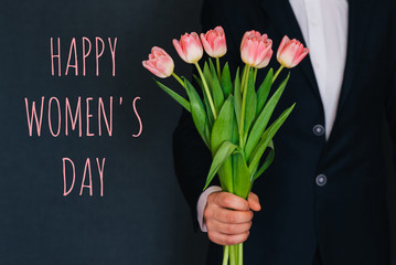 Man giving a bouquet of pink flowers tulips. Greeting card with text Happy Women's Day
