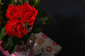 Bouquet red roses flower in glass vase on dark background and gift box, top view