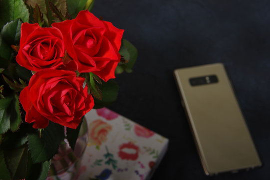 Bouquet Red Roses Flower In Glass Vase On Dark Background And Gold Smartphone No Focus, Gift Box