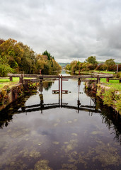 Fototapeta premium Lookin up the canal at Canal Foot, Ulverston, Cumbria. The broken lock gates are reflected in the canal on an Autumn day.