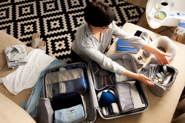 Open grey suitcase with different clothes packed for journey at home. Nordic style minimalism. woman packing bags for holidays and preparing things for vacations getting ready for travel
