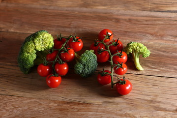 fresh cherry tomatoes on a branch and broccoli on a wooden surface