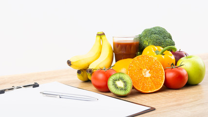 Fresh colorful vegetables, organic fruits and juice on wooden table with clipboard, paper and pen, white background with copy space for text. Cooking ingredients, healthy food and nutrition concept.