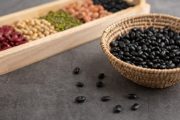 Black beans and grains in the wooden basket and in the wooden tray placed on the black cement floor. High angle view.