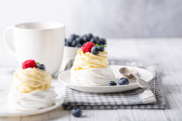 Homemade meringue cake Pavlova with whipped cream and fresh berries. White cup of coffee. Selective focus