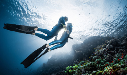 Two freedivers swim over the vivid coral reef in a tropical sea during their recreational freedive...