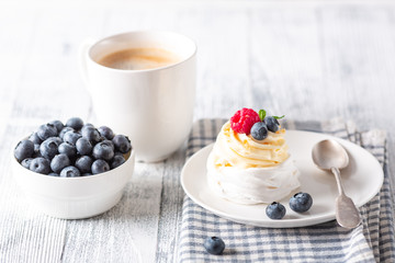 Homemade meringue cake Pavlova with whipped cream and fresh berries. White cup of coffee. Delicious dessert