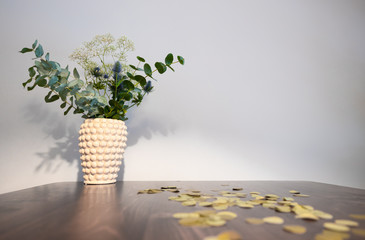 Vase with a bouquet of white and blue flowers on a wooden table before a grey background.
