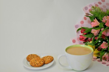 A large mug with white coffee, oatmeal cookies with cereals and a bouquet of Alstroemeria on a white background.