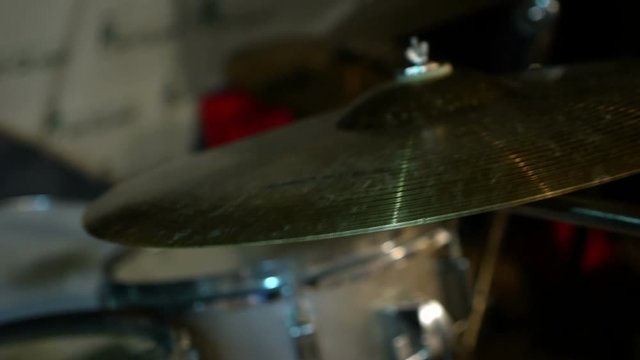Close-up of a drum kit, in the background a drummer plays in defocus, periodically striking a metal plate. Concert of a musical group