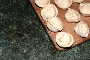 Dumplings on a wooden board on a green background. Top view on a green table with homemade food. Uncooked handmade dumplings on a wooden plate.