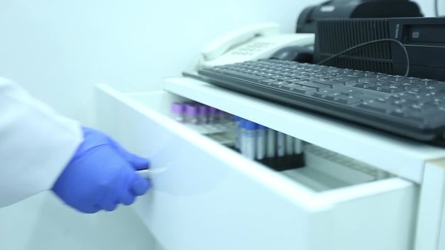 lab technician wearing a white lab coat and blue latex gloves taking out test tube from a drawer with stands 