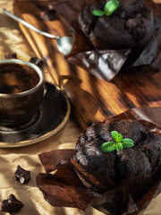 Muffins with chocolate decorated with a leaf of mint arranged on a gray paper background, close-up. Natural sunlight. Nearby is a cup of espresso and pieces of chocolate. Shallow focus