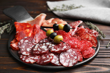 Tasty salami and other delicacies on wooden table, closeup