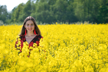 Naklejka na ściany i meble Young woman standing in yellow oilseed rape field image
