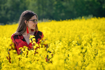Naklejka na ściany i meble Young woman with glasses standing in yellow oilseed rape field image