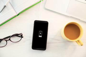 Flat lay composition with mobile phone and wireless charger on white wooden table. Modern workplace accessory
