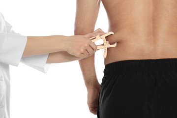 Nutritionist measuring man's body fat layer with caliper on white background, closeup