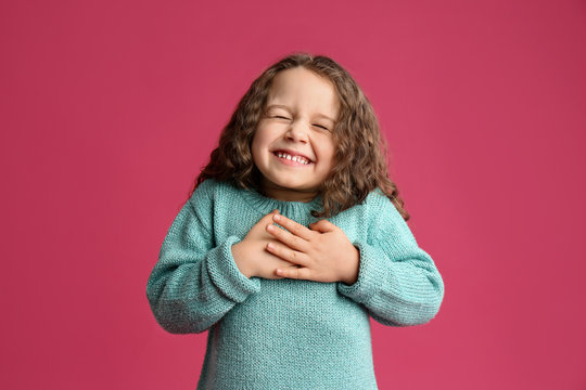 Cute grateful little girl with hands on chest against pink background